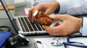 Doctor holding medicine jar and working at the laptop.