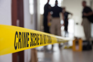 Yellow crime scene tape with investigators in the blurred background.