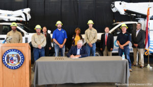 Governor Parson signing bill surrounded by workers with safety helmets on.