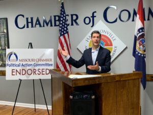 Man speaking near Missouri Chamber political action committee endorsed sign.