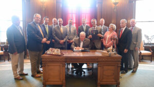 Governor Parson signing a document with numerous people next to him.