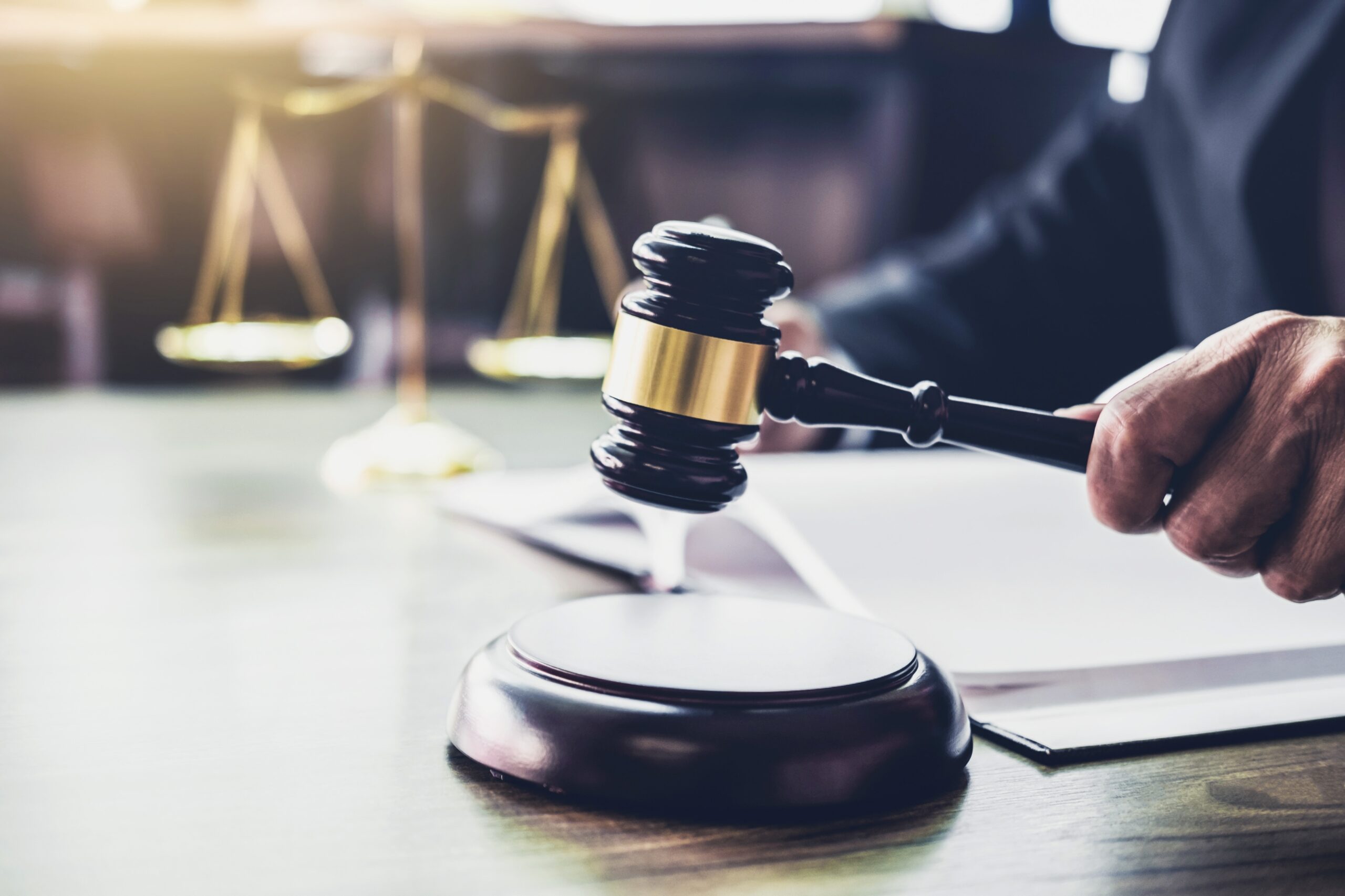 Judge with gavel in hand and scale of justice in background.