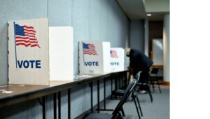 Man casting a vote in a ballot box with empty seats in the background.