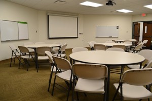 Multipurpose room with round tables and projector screen.