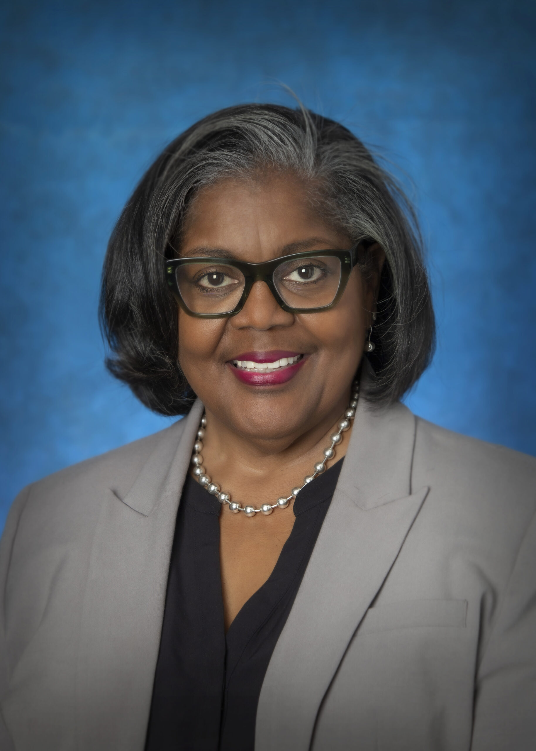 Woman smiling with grey suit, black blouse and glasses