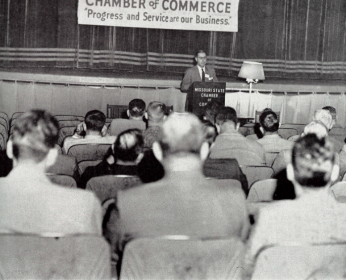 Old photograph from inside the Chamber of Commerce, with banner in the background that says 