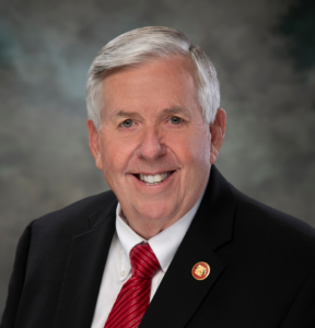 Gov. Parson in dark suit with red tie and lapel pin.