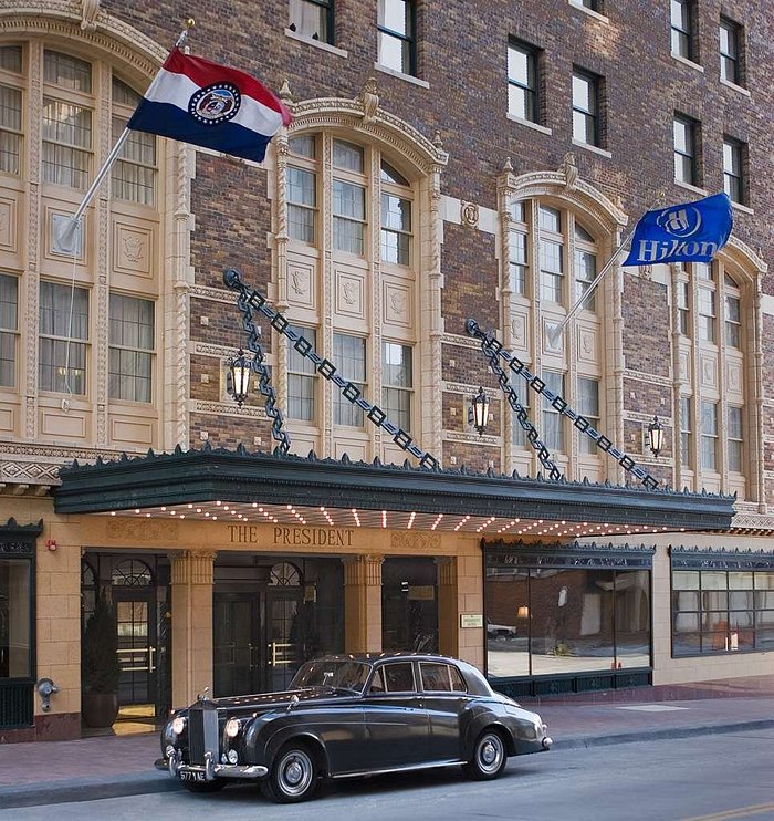 exterior image of hotel with flags, awning and old car parked out frornt