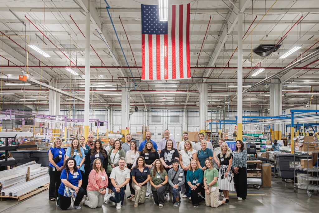 Group photo of educators smiling at H.E. Williams, Inc. with large American flag hanging from the ceiling.