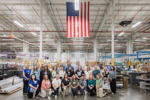 Group photo of educators smiling at H.E. Williams, Inc. with large American flag hanging from the ceiling.